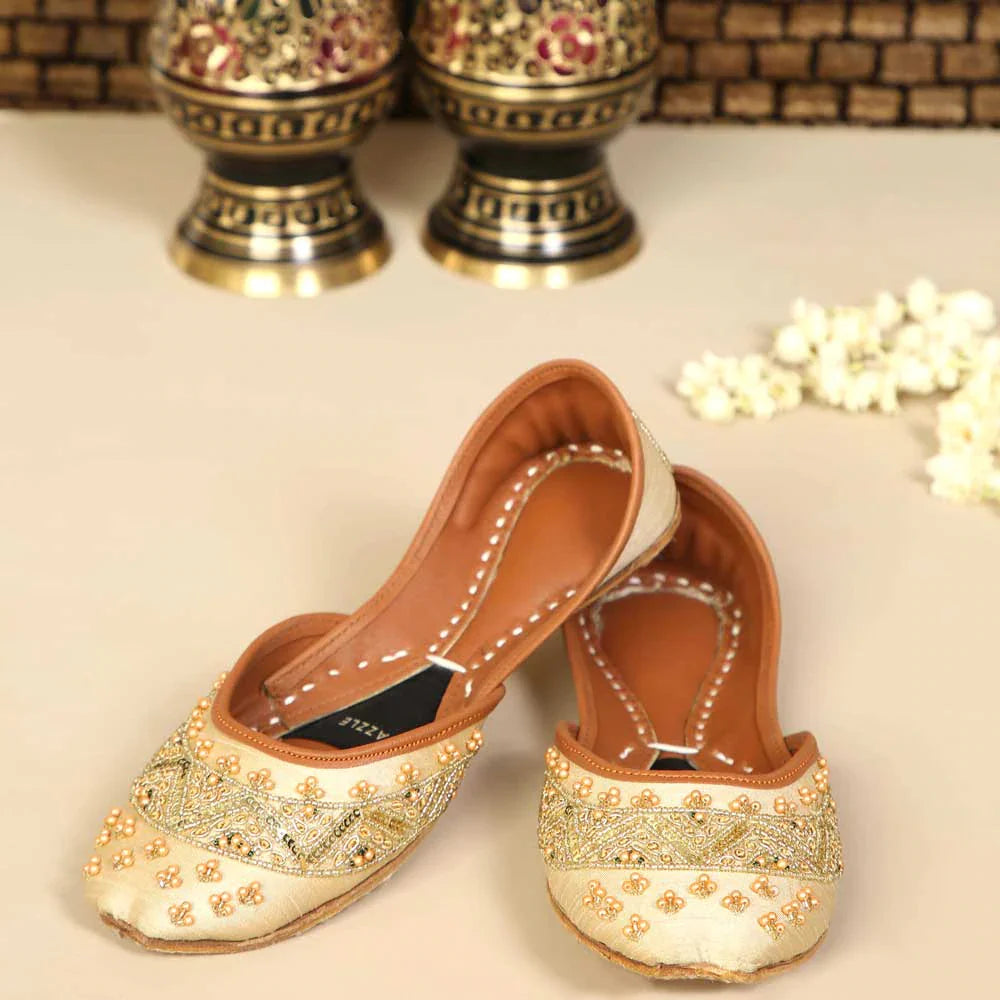 Pair of ornate flat shoes with gold embellishments on a light background
